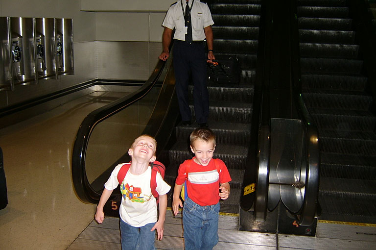 Joel and Todd get off the escalator at the airport.