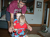 Dan helps keep Todd on the back of the tricycle as Joel peddles.