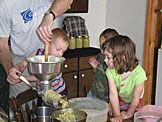 Joel cranks the applesauce machine while Todd and Madeline wait their turn.