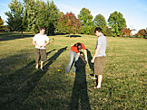 Abe and Mark watch Kirsten as she violates croquet rule 136.72, "Thou shalt not make a path for your ball to follow by altering the playing surface with your mallet."