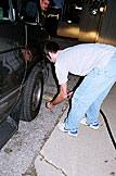 Dan checks the tire pressure of the back tires on the van while Jeremy looks on.