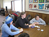 Carrie Blunier, Cecily Stieglitz, Tianna Stieglitz, and Phil Fischer play cards while Paul Fischer relaxes with a good book.